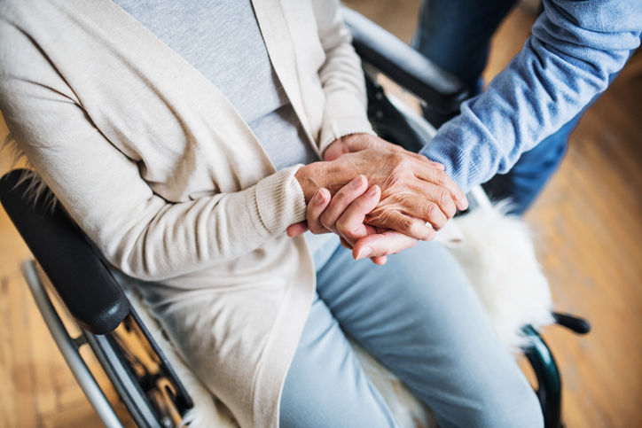 An old man and a woman in wheelchair at home, holding hands